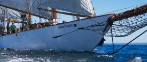 An image of a large boat while sailing, visible with full sails and the name of the ship, "Adventuress"