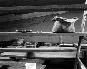 Some caulkers tools sit on a beam of wood in the foreground of a photo of a boat's hull.