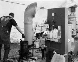 A man in overalls lifts a bucket with caulk running down the side on the deck of the Lightship Swiftsure