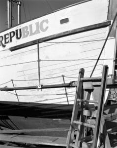 The Republic sits in dry dock with a ladder in the foreground. The name of the ship appears to be partway through being repainted.