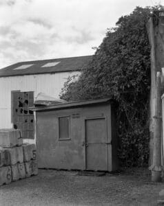 A simple shed with a wooden panel identifying it as the Oakum Loft. A small boat rests on top of the shed.