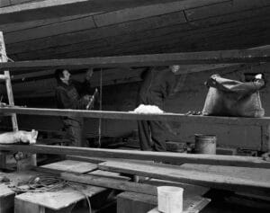 Two caulkers work on hammering long strands of thread into the gaps of the Virginia V's hull