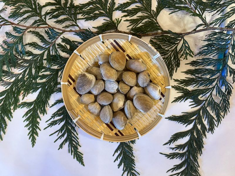 A wooden plate serving clams, with cedar bows on a white tablecloth in the background.